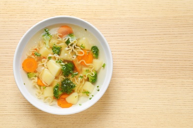 Bowl of fresh homemade vegetable soup on wooden background, top view. Space for text