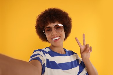 Photo of Happy young woman in sunglasses taking selfie on orange background