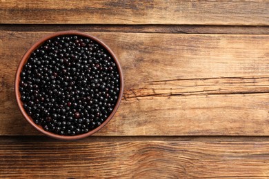 Photo of Bowl with elderberries (Sambucus) on wooden table, top view. Space for text
