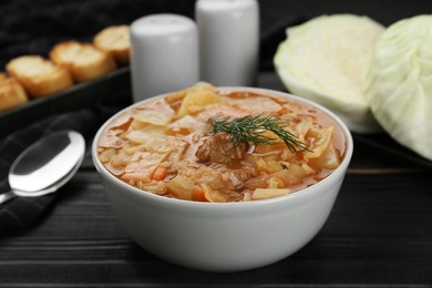 Tasty cabbage soup with meat, carrot and dill on black wooden table, closeup