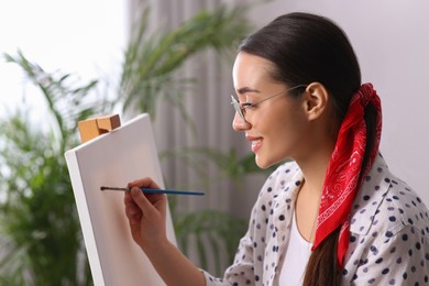 Happy woman artist drawing picture on canvas indoors