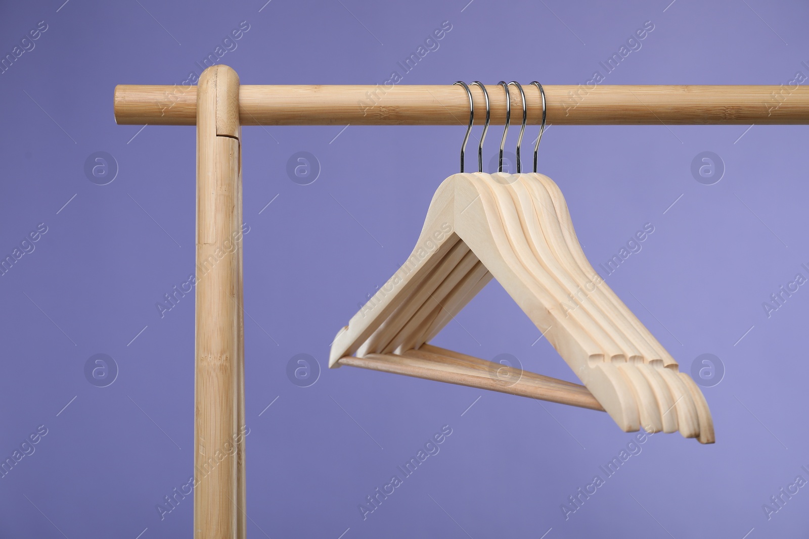 Photo of Empty clothes hangers on wooden rack against purple background