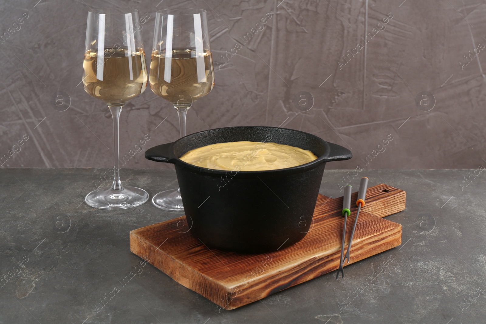 Photo of Fondue pot with tasty melted cheese, forks and wine on grey table