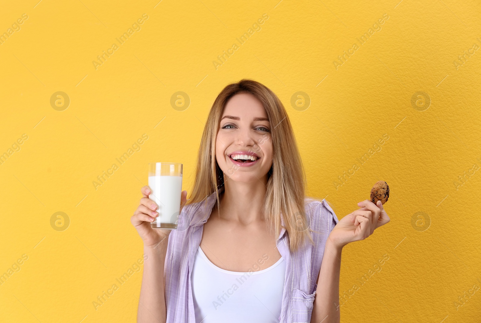 Photo of Beautiful young woman drinking milk with cookie on color background