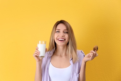 Photo of Beautiful young woman drinking milk with cookie on color background