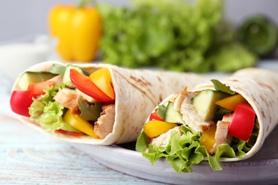 Plate with delicious meat tortilla wraps on wooden table, closeup