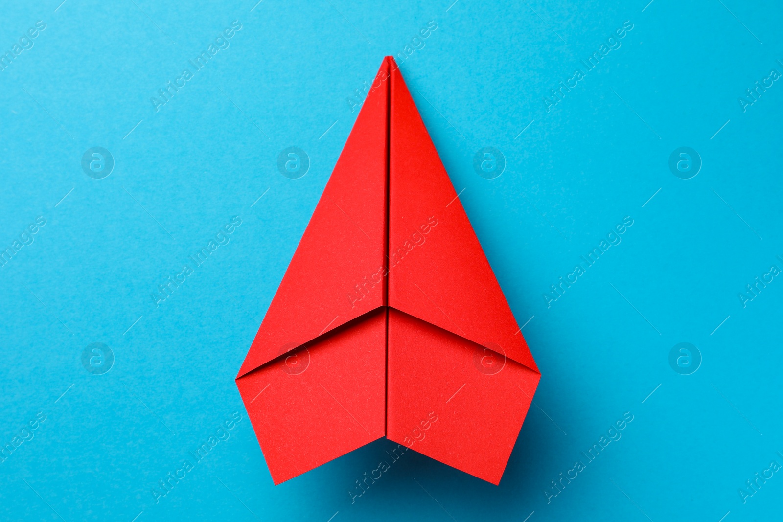 Photo of Handmade red paper plane on light blue background, top view