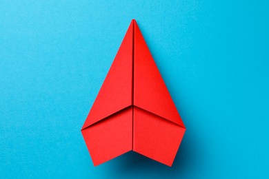 Photo of Handmade red paper plane on light blue background, top view