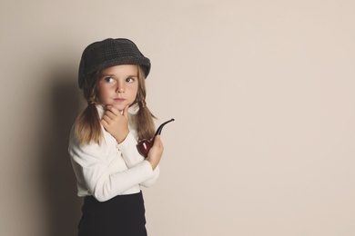 Cute little child in hat with smoking pipe playing detective on beige background, space for text
