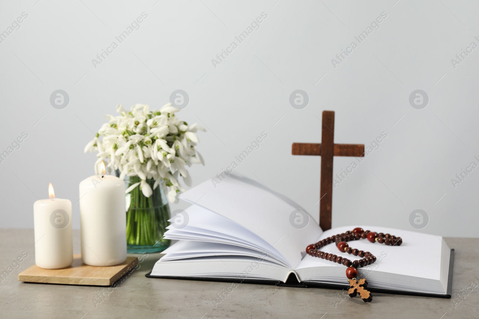 Photo of Church candles, Bible, wooden cross, rosary beads and flowers on grey table