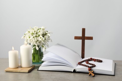 Photo of Church candles, Bible, wooden cross, rosary beads and flowers on grey table