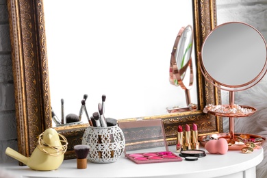 Photo of Table with beautiful mirror, cosmetics and tools in modern makeup room