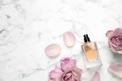 Photo of Flat lay composition with bottle of perfume and roses on white marble background, space for text