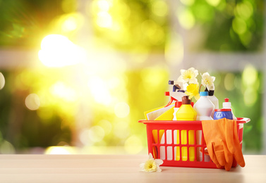 Image of Plastic basket with different detergents on wooden table against blurred background, space for text. Spring cleaning concept 