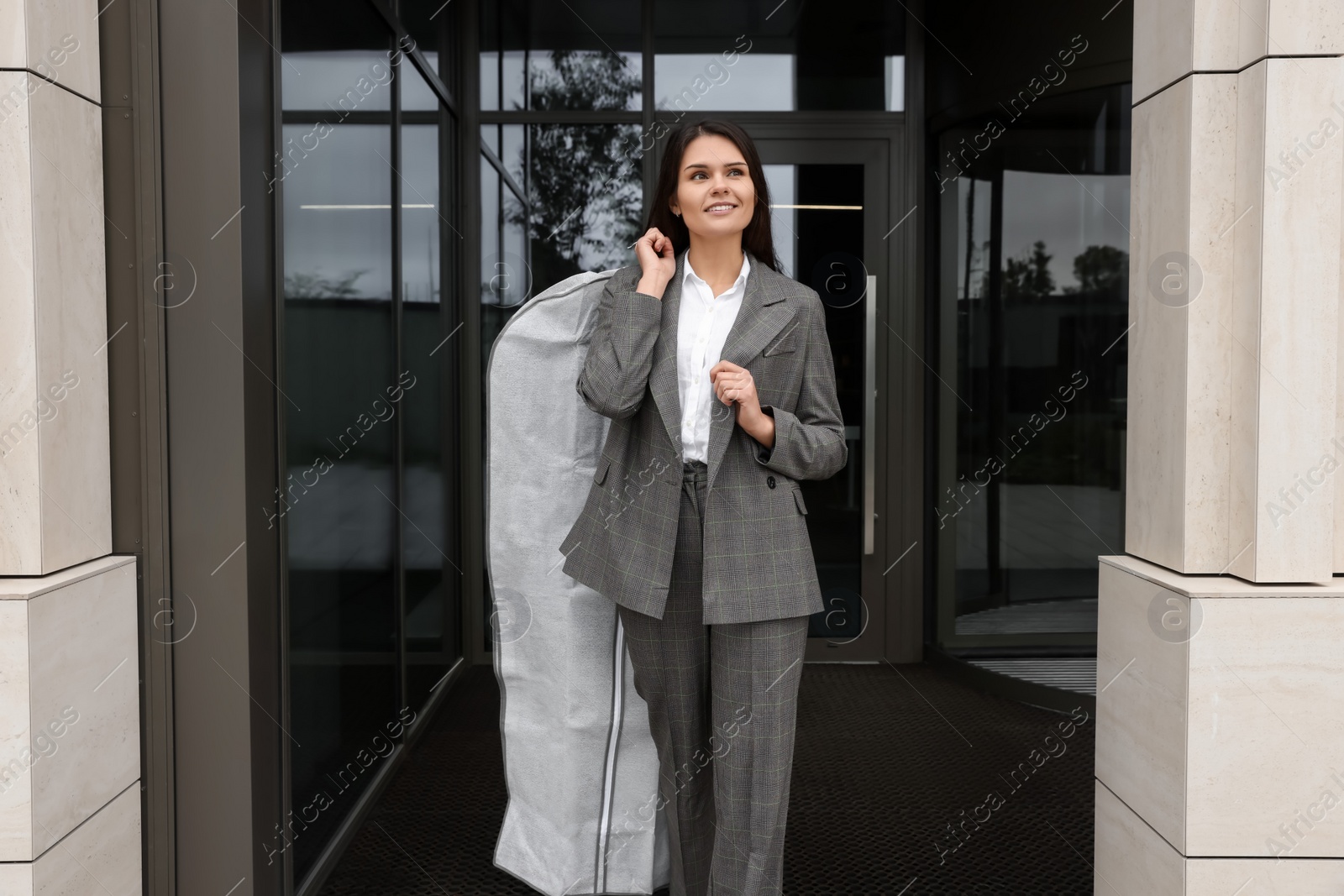 Photo of Attractive happy businesswoman holding garment cover with clothes outdoors. Dry cleaning service