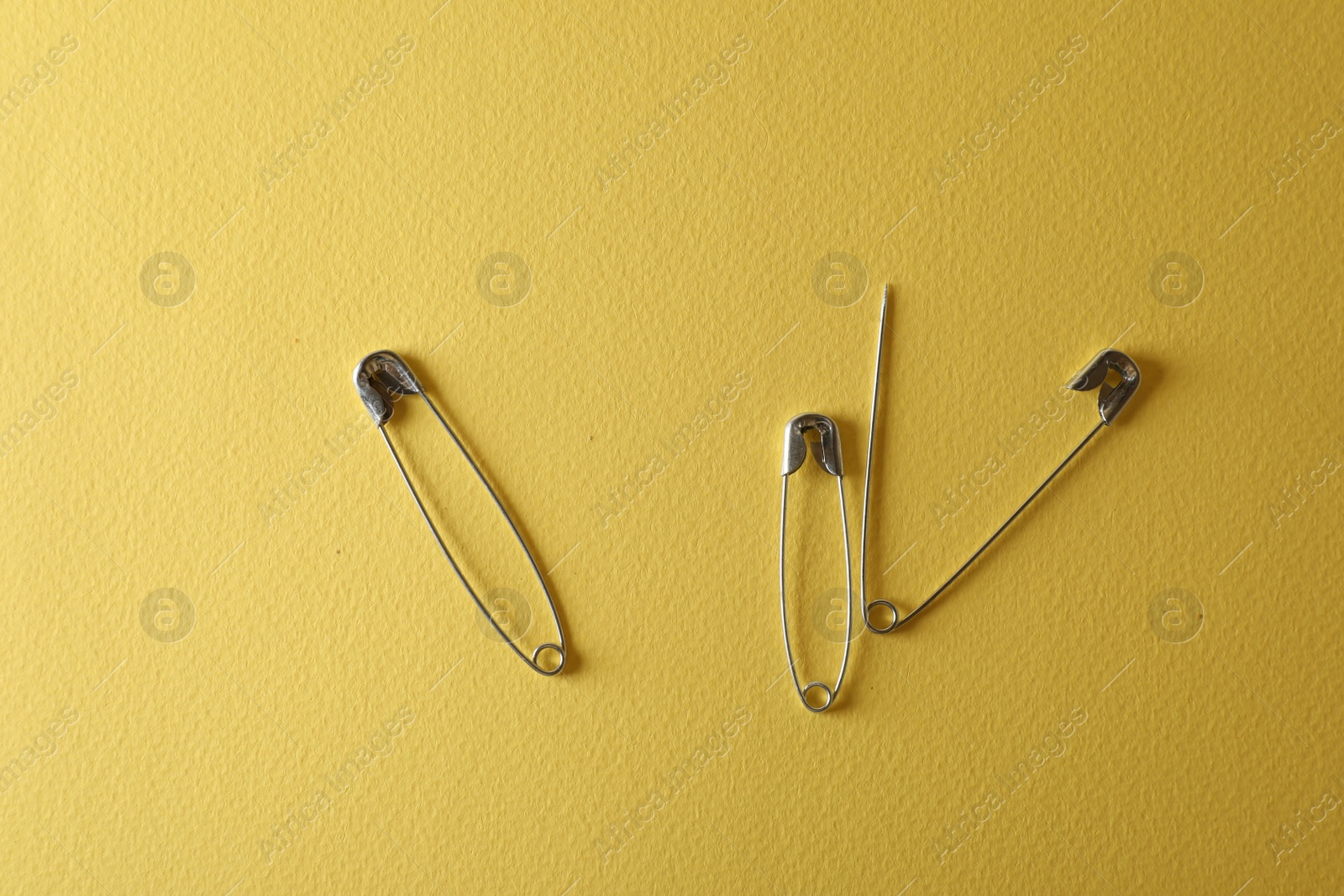 Photo of Safety pins on yellow background, flat lay