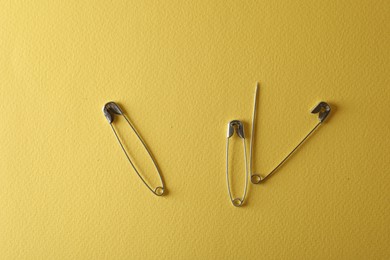Safety pins on yellow background, flat lay