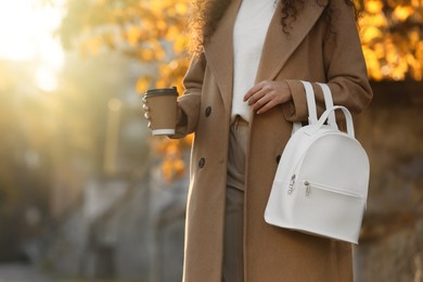 Young woman with stylish white backpack and hot drink outdoors on sunny day, closeup