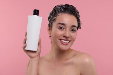 Photo of Washing hair. Portrait of beautiful happy woman with bottle on pink background