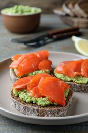 Photo of Delicious sandwiches with salmon and avocado on grey plate, closeup