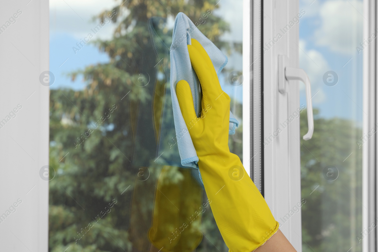 Photo of Woman cleaning window glass with rag indoors, closeup