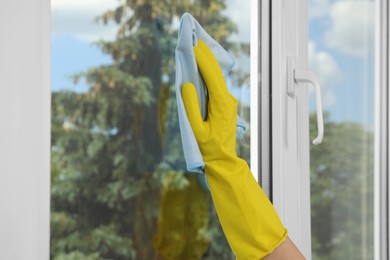 Woman cleaning window glass with rag indoors, closeup