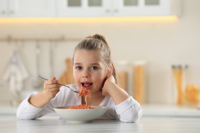 Photo of Cute little girl eating tasty pasta at table in kitchen