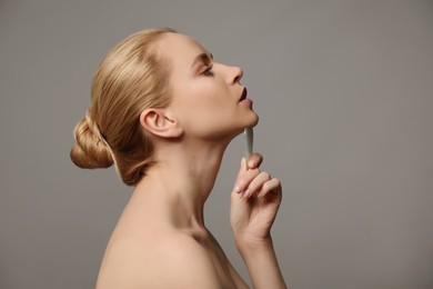 Photo of Beautiful young woman doing facial massage with gua sha tool on grey background