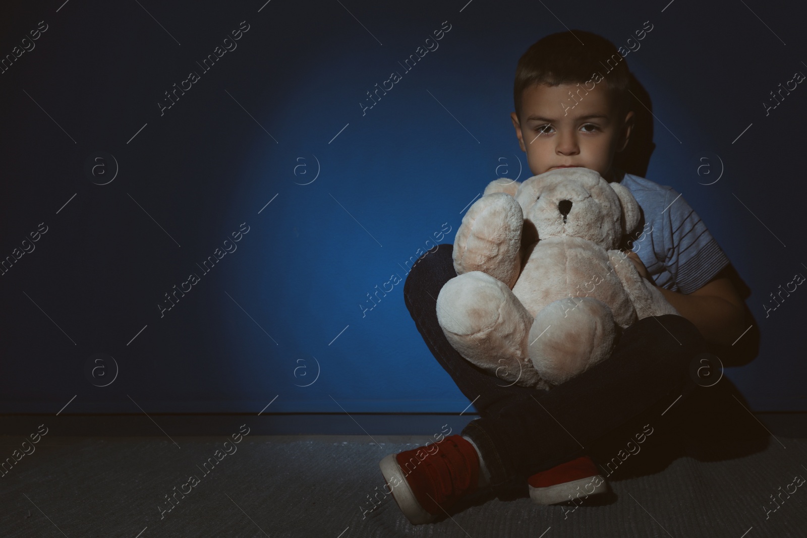 Photo of Sad little boy with teddy bear near blue wall, space for text. Domestic violence concept