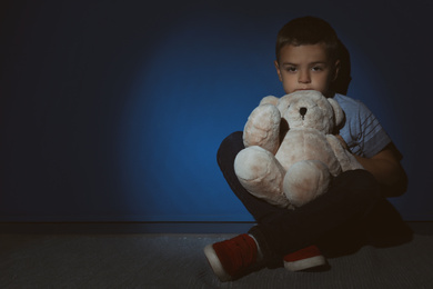 Sad little boy with teddy bear near blue wall, space for text. Domestic violence concept