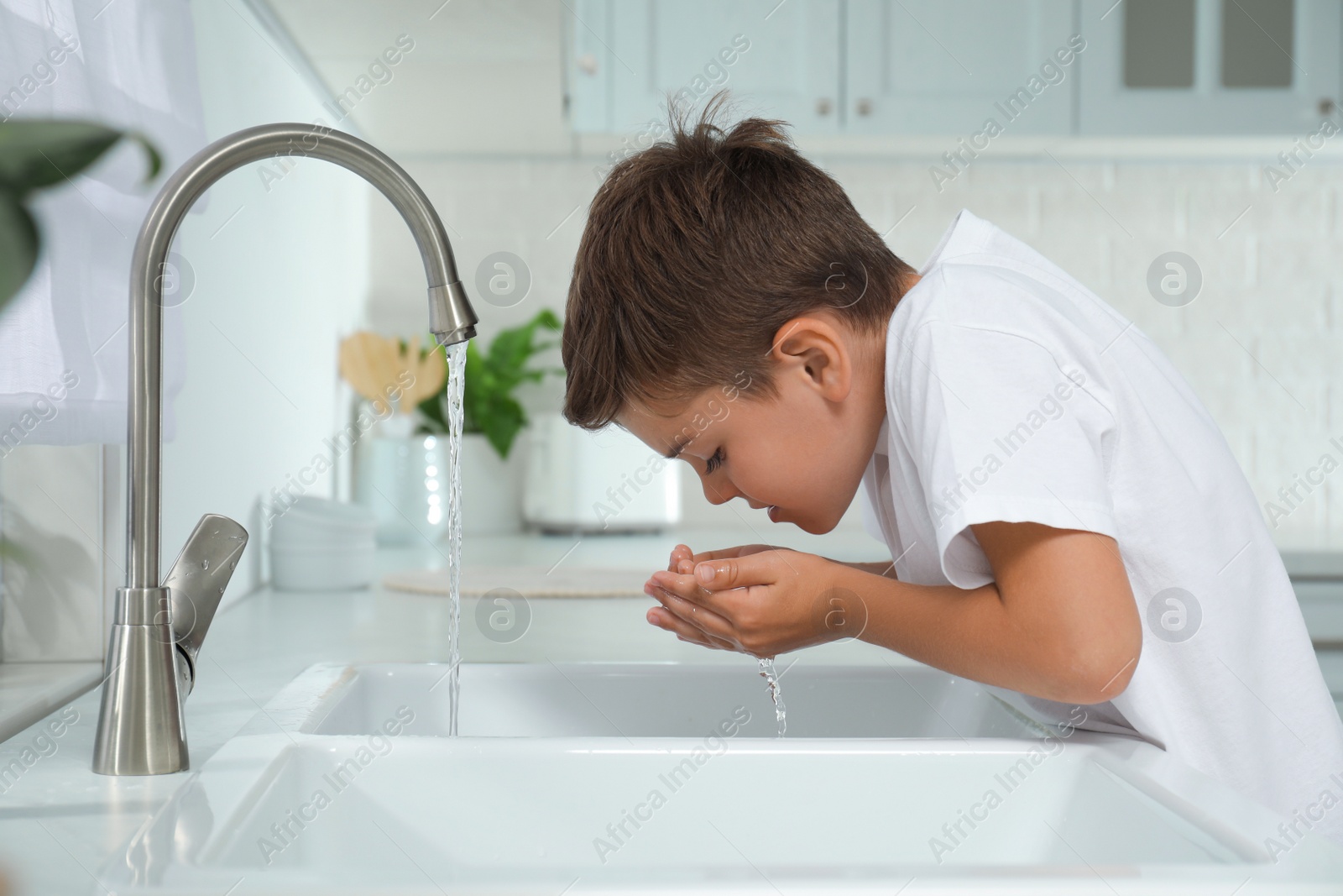 Photo of Boy drinking tap water over sink in kitchen