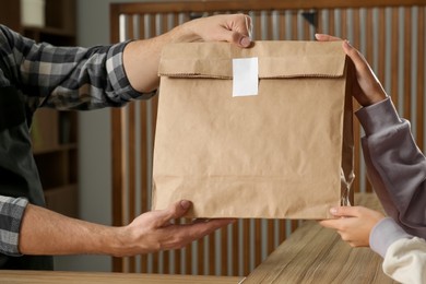 Worker giving paper bag to customer in cafe, closeup