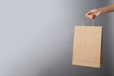 Photo of Woman holding kraft paper bag on grey background, closeup with space for text. Mockup for design