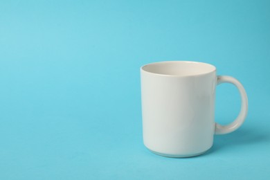 Photo of One white ceramic mug on light blue background, space for text