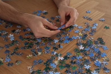 Man playing with puzzles at wooden table, closeup