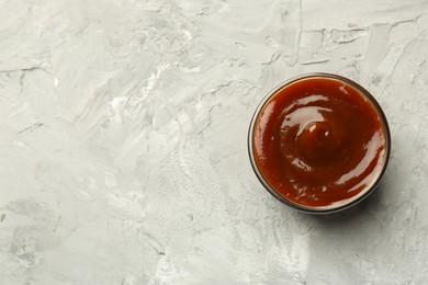 Photo of Tasty barbeque sauce in bowl on grey textured table, top view. Space for text