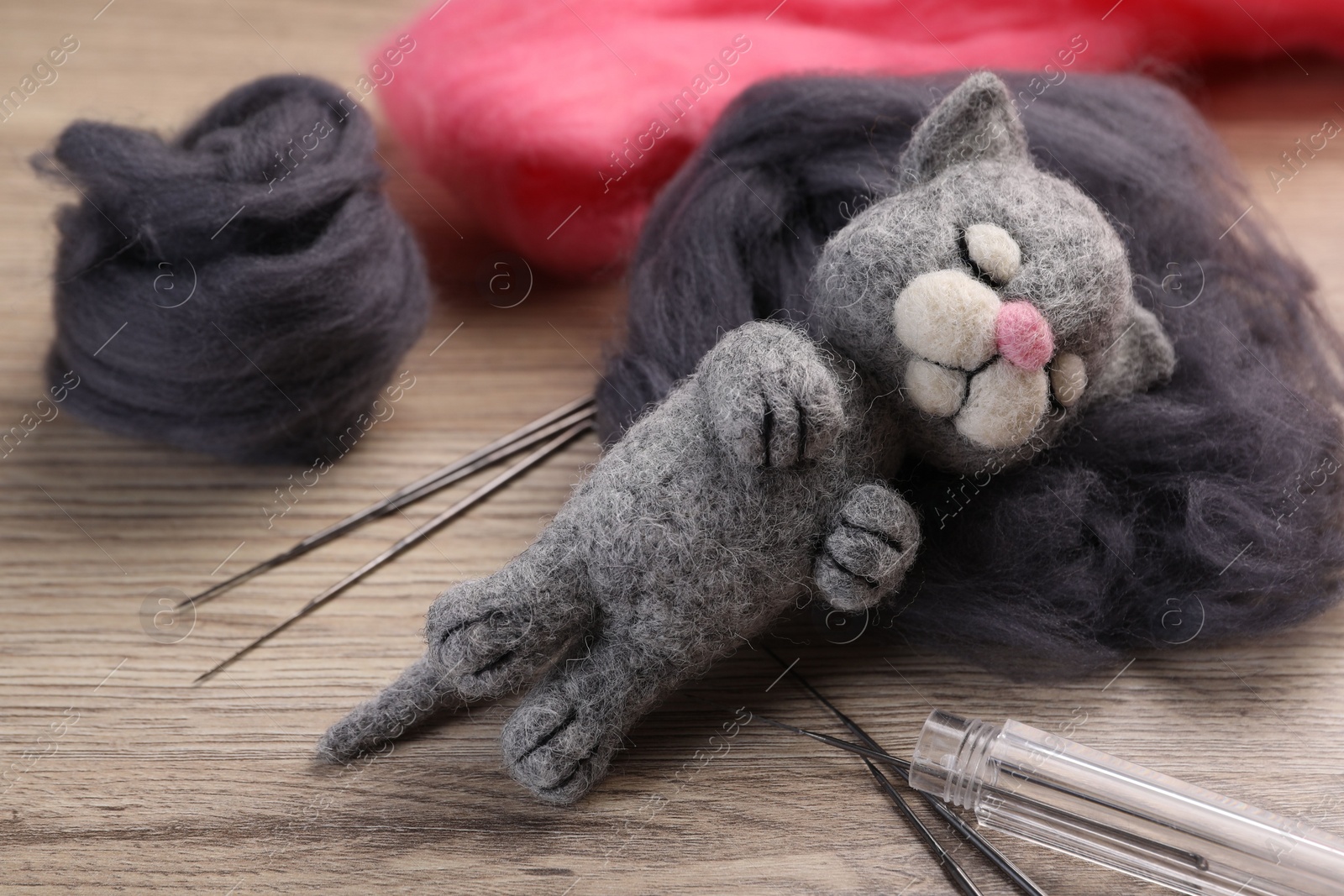 Photo of Felted cat, wool and tools on wooden table, closeup