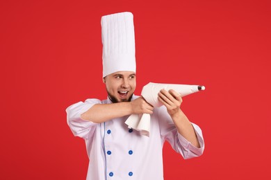 Photo of Happy professional confectioner in uniform having fun with piping bag on red background