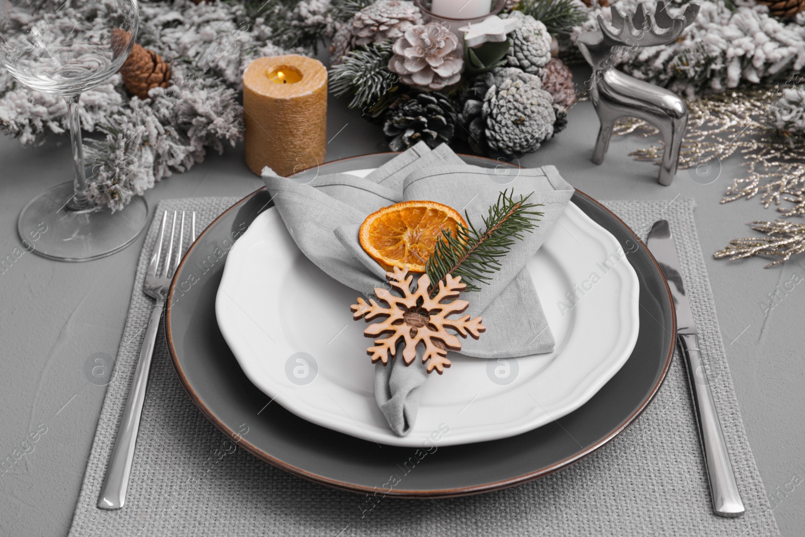 Photo of Festive place setting with beautiful dishware, fabric napkin and dried orange slice for Christmas dinner on grey table