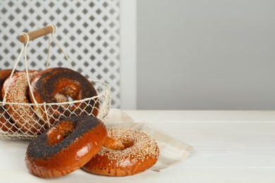 Many delicious fresh bagels on white wooden table, space for text