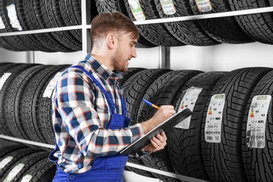 Young male mechanic with clipboard near tires in automobile service center