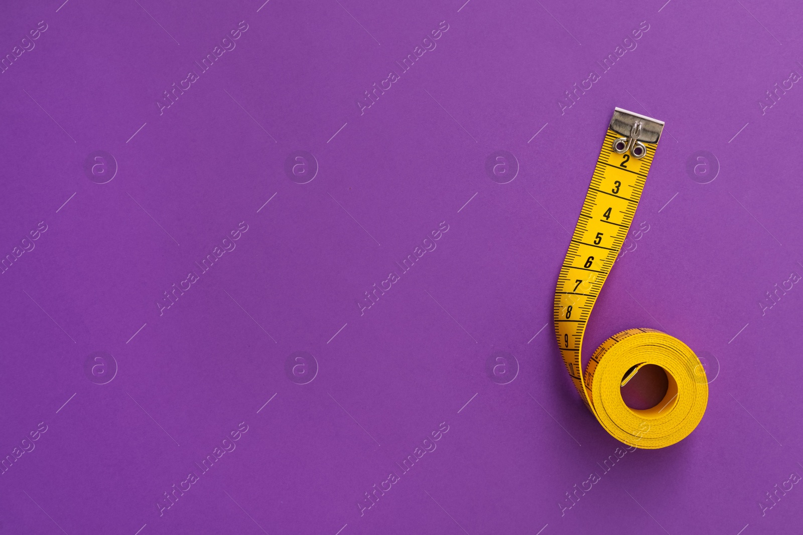 Photo of Yellow measuring tape on purple background, top view. Space for text