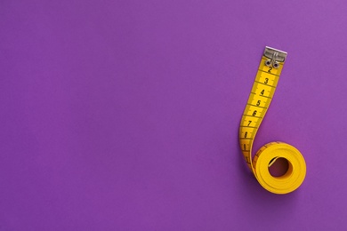 Yellow measuring tape on purple background, top view. Space for text