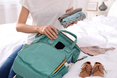 Woman packing baby accessories into maternity backpack on bed, closeup