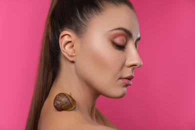 Photo of Beautiful young woman with snail on her neck against pink background