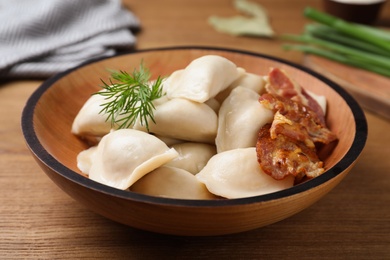 Photo of Bowl of tasty cooked dumplings on wooden table, closeup