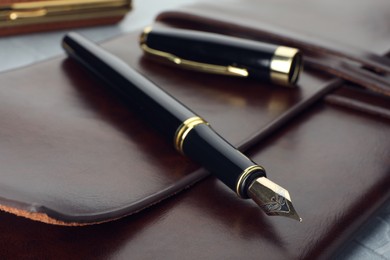 Photo of Stylish fountain pen, cap and leather notebook on grey table, closeup