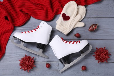 Photo of Pair of ice skates, Christmas decor, red scarf and knitted mittens on grey wooden background, flat lay