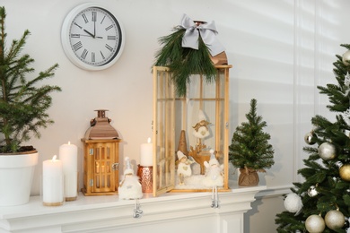 Photo of Beautiful wooden lanterns and other decorations on mantelpiece in room with Christmas tree