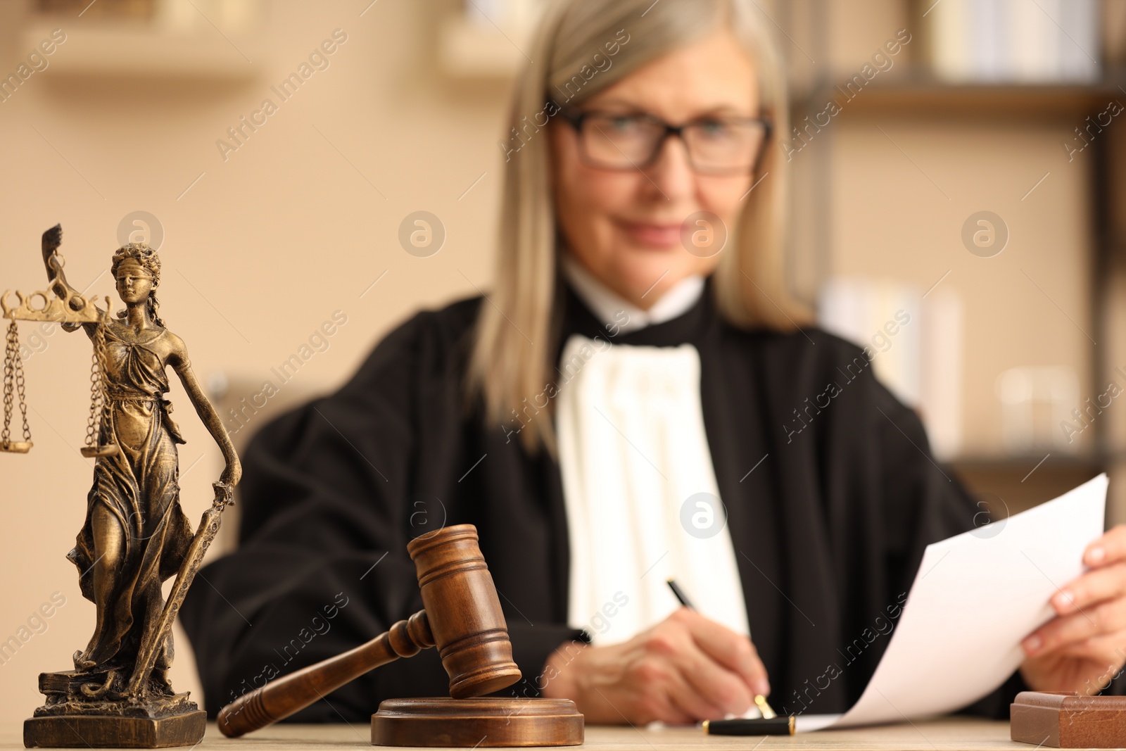 Photo of Judge working indoors, selective focus. Figure of Lady Justice and mallet on wooden table